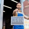 close-up view of smiling male business owner holding open sign